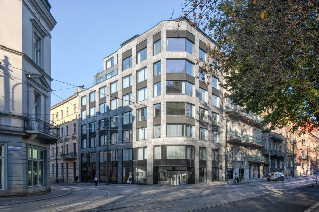 Großes Bürogebäude mit zahlreichen Fenstern, umgeben von Straßeninfrastruktur, Fahrzeugen, Fußgängern, Bäumen und einem bewölkten Himmel.