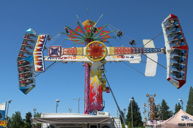 Kirmesfahrt mit Menschen auf einem Markt, umgeben von Zelten, Bannern, Pfählen, Lichtern, Bäumen und einem sichtbaren Himmel.