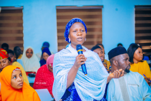 Eine Frau in einem blauen Kleid spricht vor einer sitzenden Gruppe, einige halten Stifte, wahrscheinlich in einer Kirche und diskutiert die Rechte von Frauen in Nigeria.