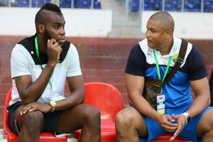 Zwei Männer in einem Stadion, einer trägt ein weißes und schwarzes T-Shirt mit blauen Shorts, der andere trägt eine ID-Karte.
