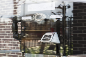 Ein altmodisches Münztelefon steht auf einem Glasfenster, mit einer Wand im Hintergrund.