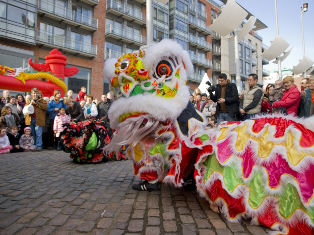 Eine Löwentanz-Vorführung während eines Chinesischen Neujahrsfestes in Amsterdam, mit einer Zuschauermenge und Gebäuden im Hintergrund.