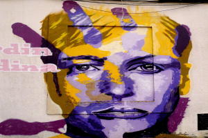 Ein leuchtendes, farbenfrohes Wandgemälde eines Frauenkopfs auf einem Gebäude in Berlin, Deutschland, mit detaillierten Zügen und fettem Text.