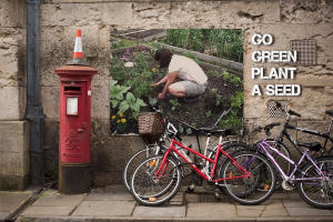 Fahrräder in der Nähe einer Briefkasten mit einer Sicherheitskegel darauf, eine Wand mit einem Plakat und Text im Hintergrund und ein Weg am unteren Rand des Bildes.