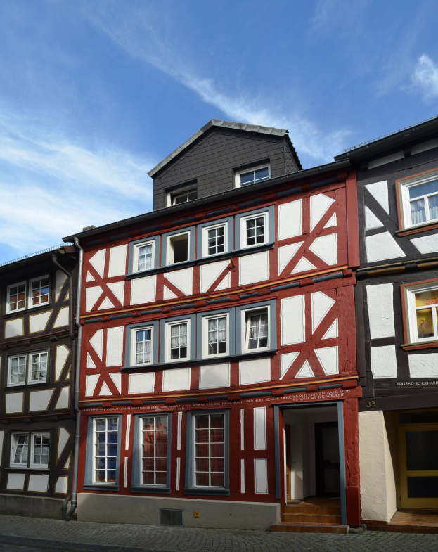 Eine Reihe von Fachwerkhäusern in Heidelbergs altem Stadtkern mit sichtbaren Fenstern und Türen, vor einem Himmel mit weißen, flauschigen Wolken.