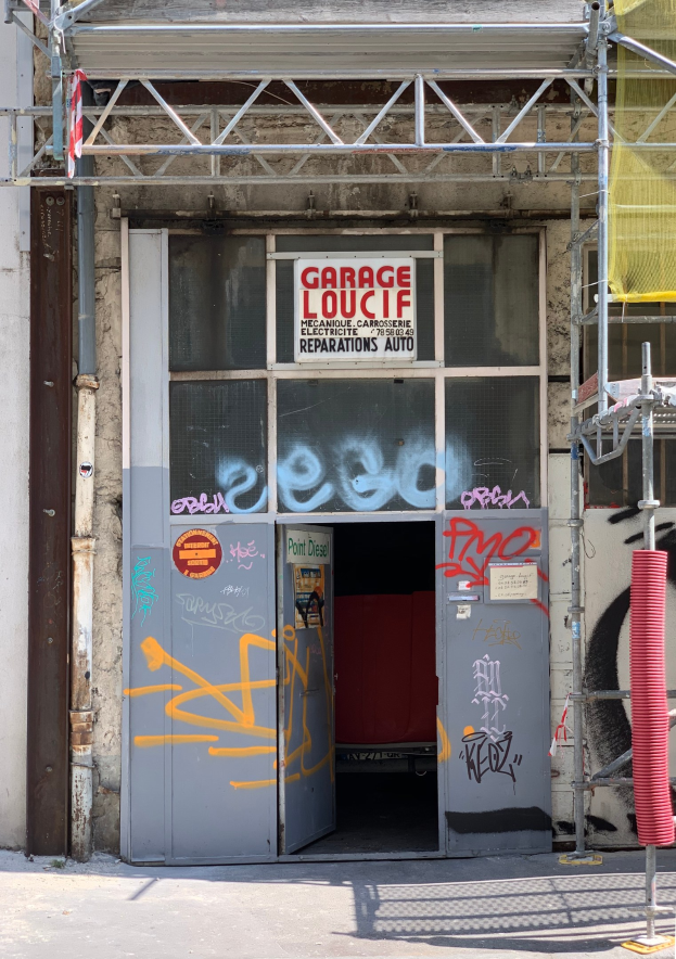 Gebäude mit Graffiti-bedeckter Wand, einer Tür, einer Texttafel, Metallstangen, einem Rohr, einem gelben Tuch und einer Straße unten.