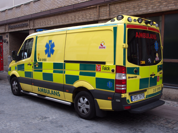 Ambulanz vor einem Backsteingebäude mit Feuerlöscher auf der linken Seite geparkt, auf der Straße mit Text auf dem Gebäude im Hintergrund.