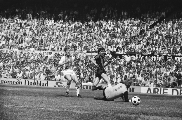 Schwarz-weißes Foto von Männern, die auf einem Feld Fußball spielen, mit Zuschauern im Hintergrund und einer "Bundesliga 1978-79 Ajax 1-1 Hannover 96"-Tafel.