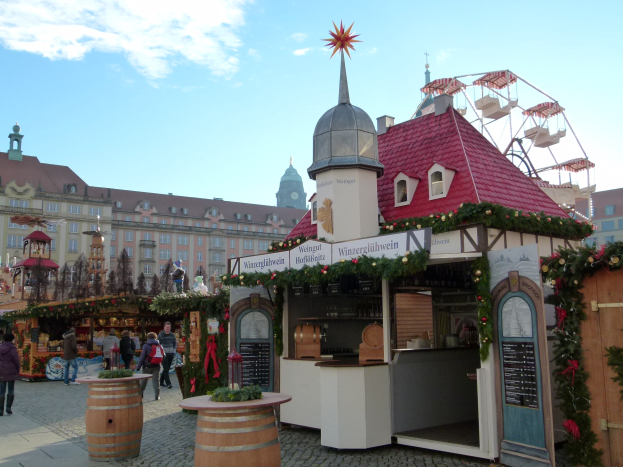 Ein geschäftiger Weihnachtsmarkt in Nürnberg, Deutschland, mit Menschen um dekorierte Buden, festliche Lichter, Schmuck, Gebäude mit Fenstern, ein Riesenrad und ein bewölkter Himmel, mit einer Tafel mit Text auf der rechten Seite.