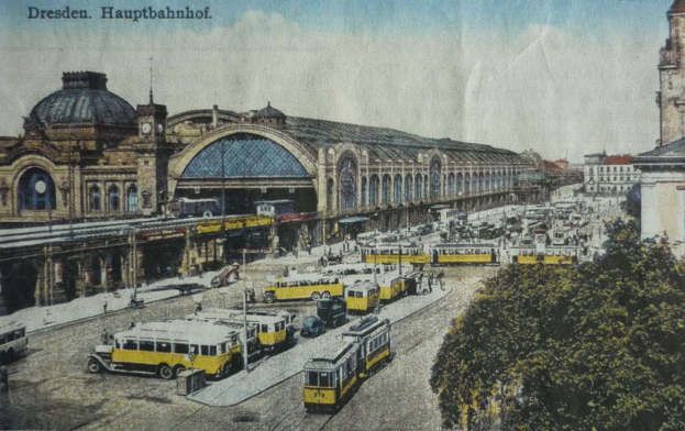 Eine sepiafarbene Postkarte zeigt den Dresdner Hauptbahnhof mit Pferdefuhrwerken, Passanten, Bäumen, Gebäuden und einem bewölkten Himmel.