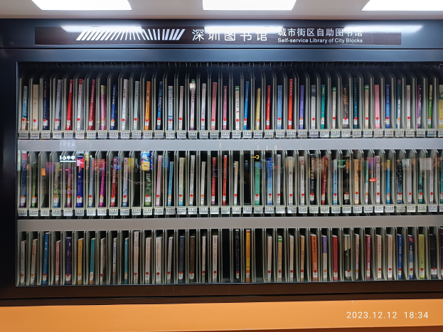 Eine gut beleuchtete Bibliothek mit hohen Bücherregalen voller Bücher, eine Tafel mit Text und ein Wasserzeichen unten, das an eine Selbstbedienungsbibliothek in Stadtblocks erinnert.