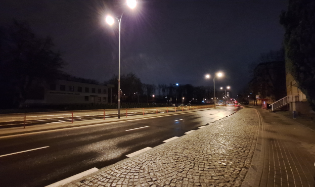 Eine nächtliche Straßenansicht mit Laternen, die die Straße, Gehwege, Geländer, Bäume, Gebäude und andere Gegenstände beleuchten, mit dem Himmel im Hintergrund.