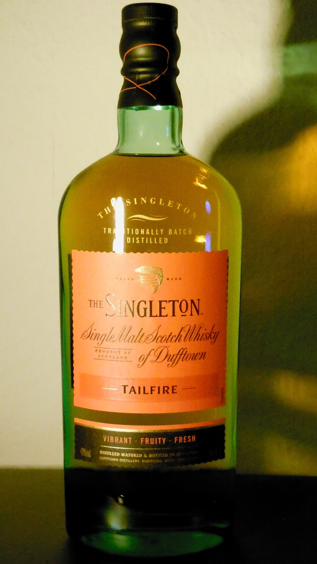 Eine tiefe bernsteinfarbene Flasche Singleton of Dufftown Tailfire Single Malt Scotch Whisky mit einem schwarzen Etikett, das seinen Namen und ein Wappen mit einem Löwen und einer Burg zeigt.