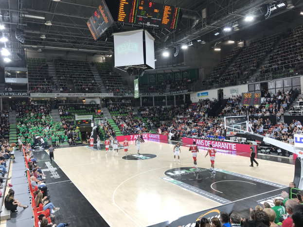 Basketballspiel zwischen Asvel und Galatasaray in einer großen Halle mit Zuschauern, Anzeigetafeln und Deckenbeleuchtung.