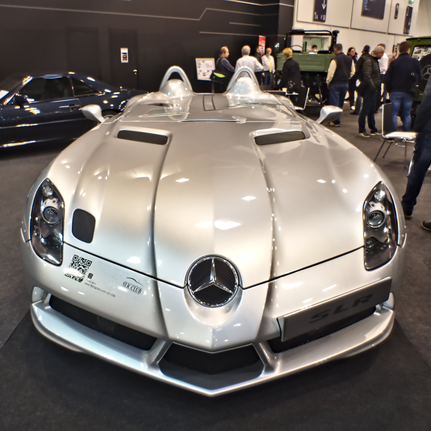 Ein Mercedes-Benz SLR McLaren Roadster wird auf dem Genfer Automobilsalon präsentiert, umgeben von mehreren Bewunderern, während die Ausstellungswände mit Tafeln und Lichtern geschmückt sind.