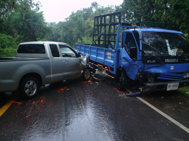 Ein demolierter Lkw mit eingedrückter Front und verbeulter Karosserie am Straßenrand, umgeben von Bäumen unter einem klaren blauen Himmel.