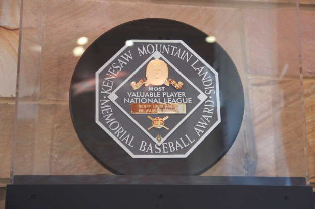 Schwarze Plakette an einer Gebäudewand mit "Mountain Lands Memorial Baseball Award"-Text, vor einem Hintergrundwall.