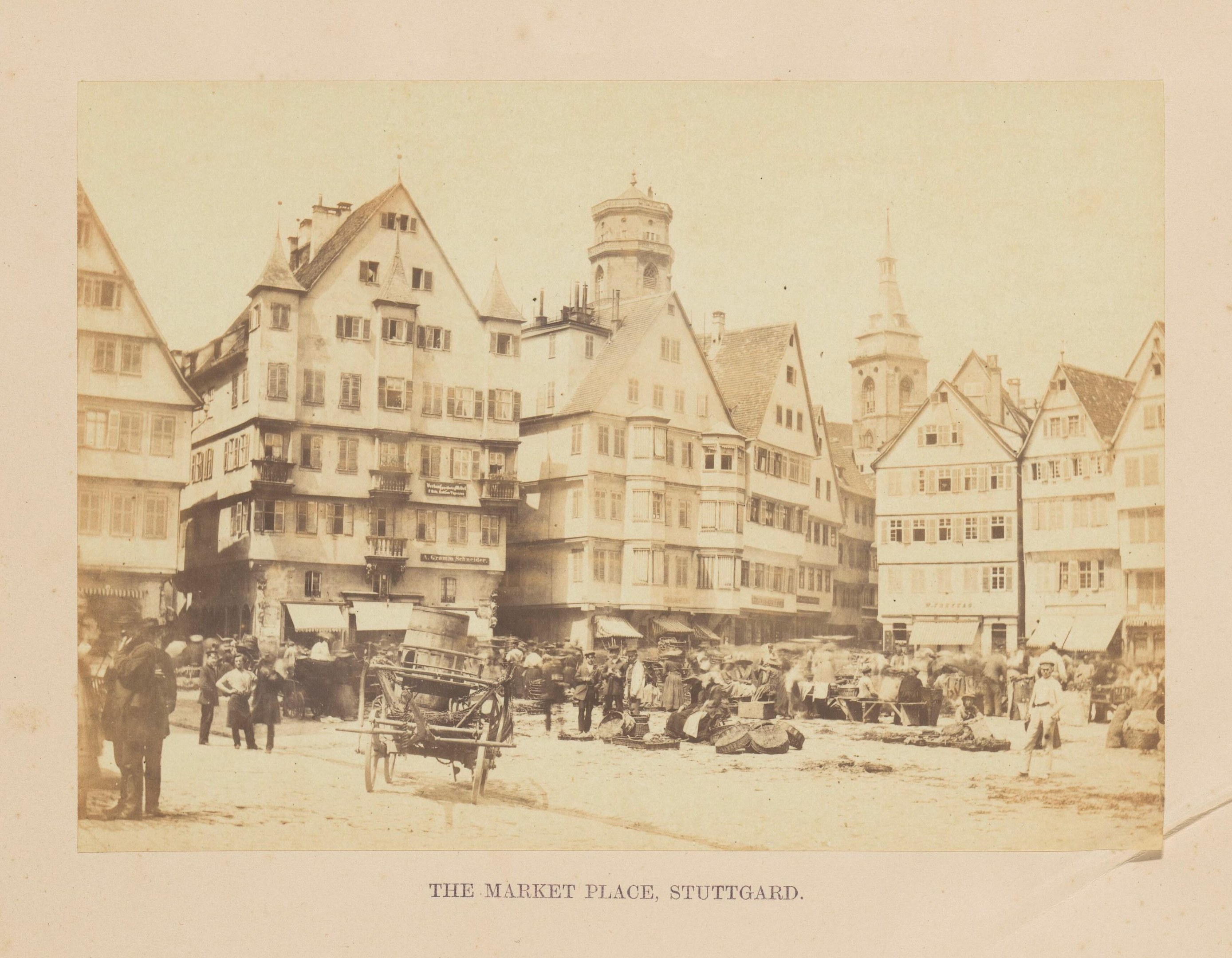 Alte Fotografie eines belebten Marktplatzes in Stuttgart, Deutschland, mit mehrstöckigen Gebäuden, Fußgängern, horse-drawn carts, und verschiedenen Marktständen; gefadedete Schrift am unteren Rand.