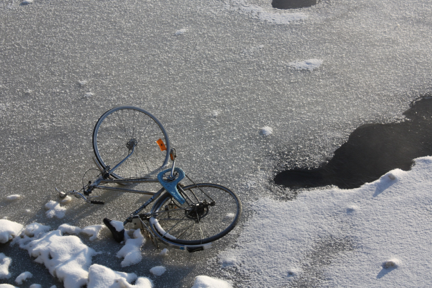 Ein Fahrrad liegt im Schnee neben einer Pfütze, mit Schnee bedeckt.
