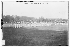 Eine Gruppe von Menschen, einige mit Gewehren in der Hand, in Formation vor Bäumen, Hügeln und einem bewölkten Himmel posierend; der Text "cadets on parade west point" erscheint oben.