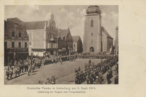 Ein Schwarz-Weiß-Foto eines Umzugs in Insterburg am 5. September 1914, das viele Menschen zeigt, einige stehen und einige gehen, mit Gebäuden im Hintergrund und Text am unteren Rand des Bildes.