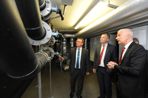 Vier Personen auf der rechten Seite, drei mit Jacken, mit gro├čen Rohrleitungen auf der linken Seite.