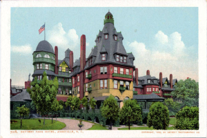 Eine alte Postkarte zeigt das Battery Park Hotel in Asheville, North Carolina, ein großes Gebäude mit einer Fahne oben, umgeben von Bäumen, Pflanzen, Gras und einem Weg, mit Text unten.