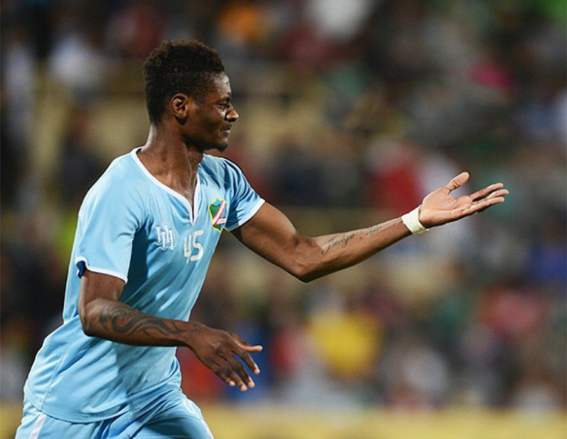 Ein Fussballspieler in einem blauen Trikot feiert nach einem Tor mit ausgestreckten Armen, mit einem unscharfen Hintergrund.