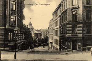 Ein altes Schwarz-Weiß-Foto einer Stadtstraße in Göteborg, Carl Gustavsgatan, mit Menschen, die auf der Straße gehen, Laternenpfählen, Bäumen, Gebäuden mit Fenstern und einem bewölkten Himmel im Hintergrund; Text ist oben auf dem Bild zu sehen.