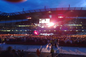 Ein Konzertsaal mit Menschen, Scheinwerfern und einer Projektionswand.