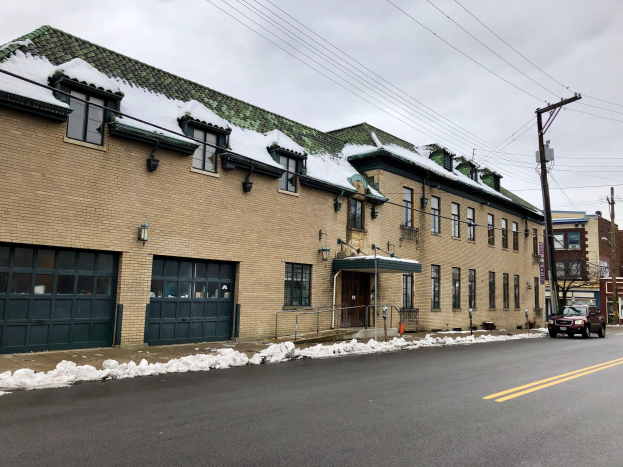 Großes Ziegelgebäude mit grüner Dachfläche an einer Straßenkreuzung, umgeben von Fahrzeugen, Schnee, Strommasten, Bäumen und einer bewölkten Himmel, identifiziert als die ehemalige Feuerwache St. Louis.