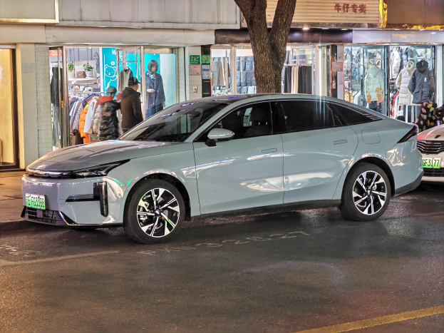 Ein Mitsubishi Lancer EV-Elektroauto, das nachts auf einer Straße geparkt ist, umgeben von Gebäuden, Geschäften, Schaufensterpuppen, Schildern und Lichtern.