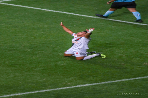 Ein Fußballspieler kniet auf dem Boden und streckt die Arme aus, trägt eine Sportuniform und Schuhe.