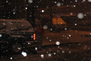 Eine dunkle Szene mit Schneefall und zwei Fahrzeugen auf einer Straße.