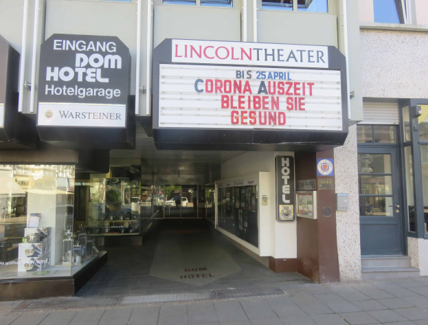Das Lincoln Theater in Berlin, Deutschland, mit Glasfenstern und -türen und einer Texttafel draußen sowie einer belebten Stadtlandschaft drinnen.