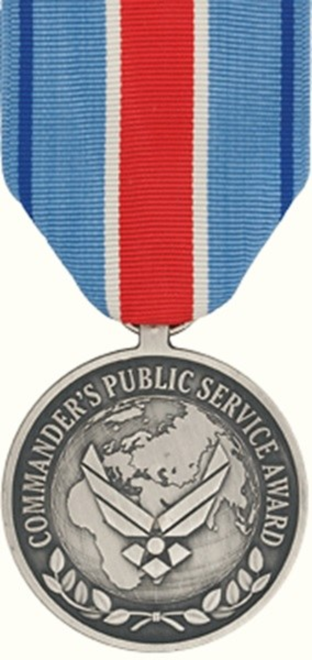 Eine Silbermedaille mit einem rot-weiß-blauen Band, auf dem 'Commander's Public Service Award' steht, vor einem weißen Hintergrund.