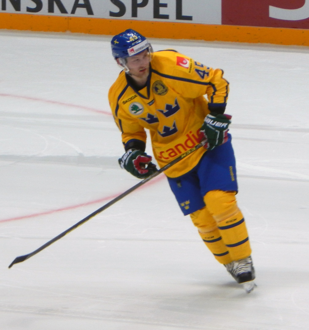 Eishockeyspieler in Bewegung auf dem Eis, mit Schutzausrüstung und Hockeystock, mit einem textgefüllten Board im Hintergrund.