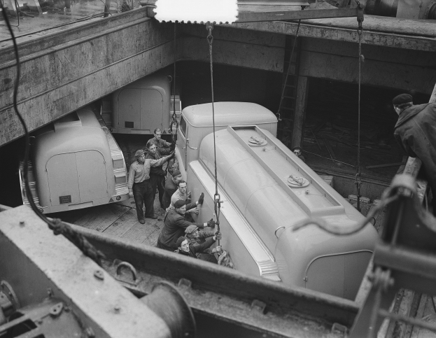 Schwarzes und weißes Bild von Männern, die an einem Truck in einer Fabrik arbeiten, mit anderen Fahrzeugen im Hintergrund.