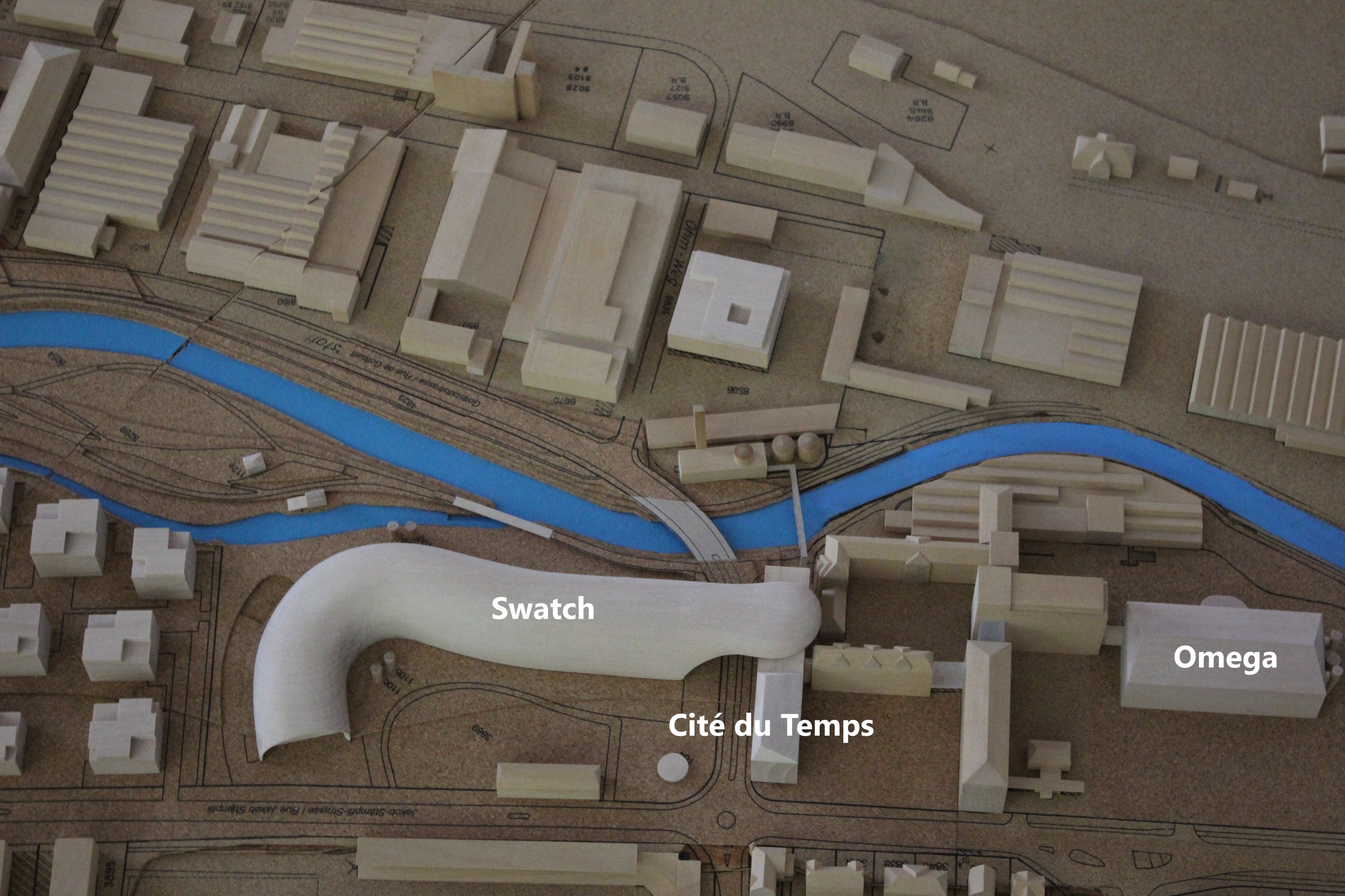 Ein Miniaturmodell einer Stadtlandschaft mit einem Fluss, Gebäuden, Straßen und Textbeschriftungen.