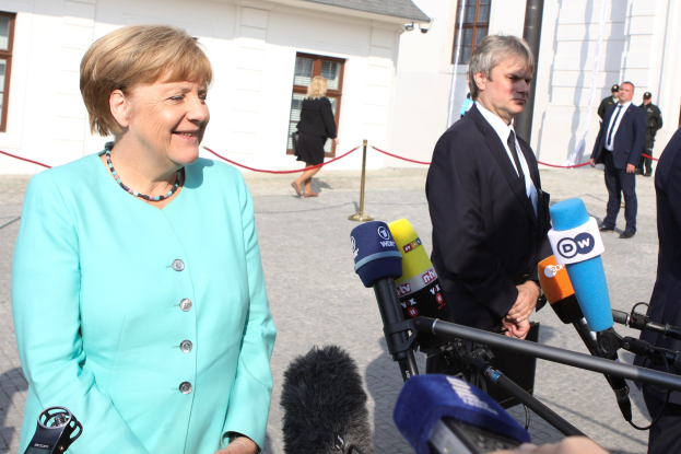 Bundeskanzlerin Angela Merkel spricht mit Reportern im Freien vor einem Gebäude mit Fenstern.