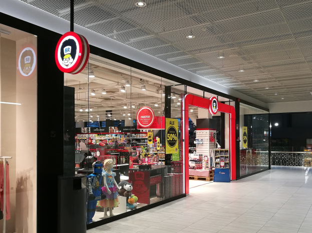 Ein moderner Spielwarenladen mit Glaswänden, sichtbarem Boden und Deckenlicht, Schaufensterpuppen und verschiedenen Spielzeugen.