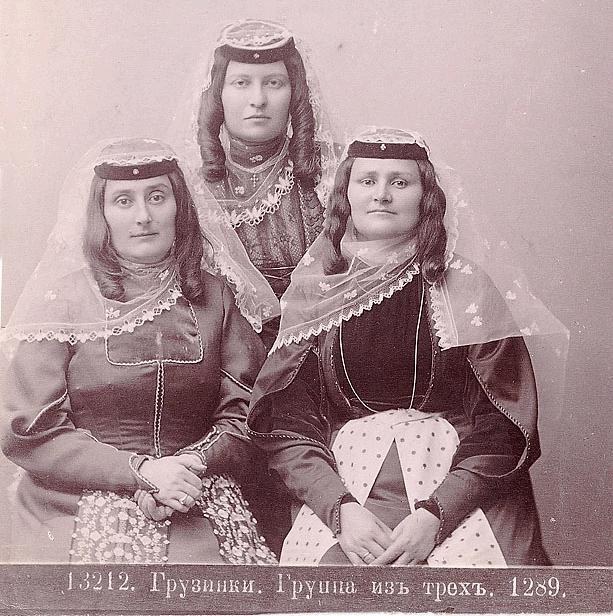 Drei Frauen in traditionellen russischen Hochzeitskleidern mit aufwendiger Stickerei und Perlen stehen vor einer weißen Wand in einem Schwarz-Weiß-Foto.