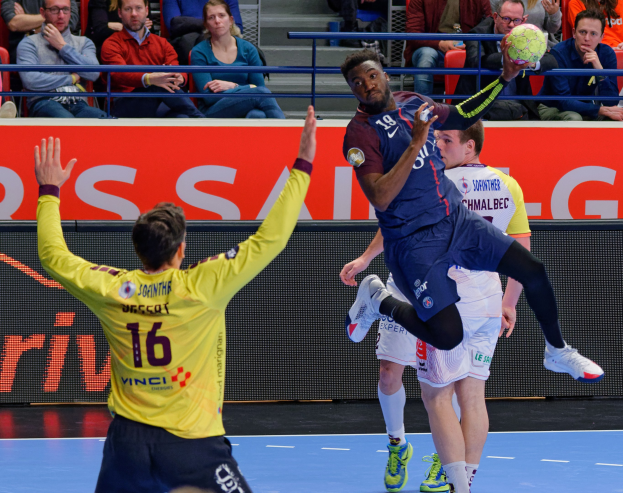 Mannergruppe spielt Handball auf einem Court mit einem Ball in der Luft, in einer Stadionatmosphäre mit Zuschauern und einem Anzeigeboard, das "Futsal-Weltmeisterschaft 2019 - Paris Saint-Germain vs Bordeaux" anzeigt.
