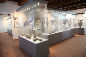 Ein Raum voller Glasvitrinen mit verschiedenen Keramikgegenständen wie Tellern, Tassen, Untertassen und Vasen, beleuchtet von Deckenlampen, mit einer informativen Tafel an der linken Wand zum Thema 'The Art of Ceramics' Ausstellung im Museum of Fine Arts in San Francisco, Kalifornien.