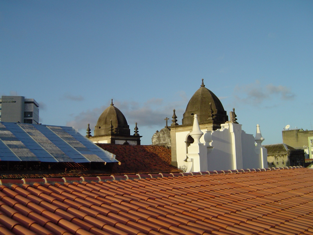 Stadtansicht mit mehreren Geb├Ąuden im Vordergrund und einem klaren blauen Himmel im Hintergrund, mit Solarpanelen auf dem Dach eines Geb├Ąudes.