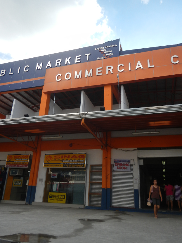 Ein öffentliches Markt-Geschäftszentrum mit Menschen davor, mit Text an dem Gebäude und einem sichtbaren Himmel oben.