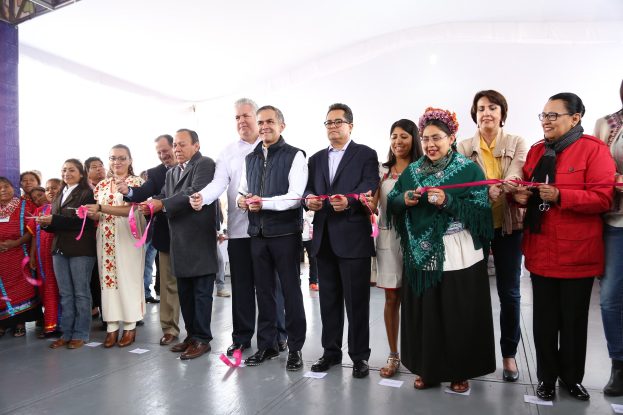Menschen schneiden ein Band bei einer Zeremonie vor einer Menge, mit Papieren auf dem Boden und einem weißen Tuch im Hintergrund.