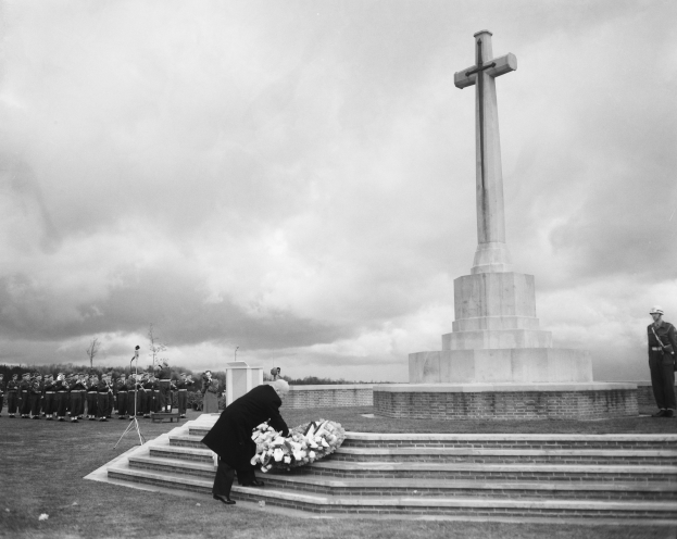 Ein Mann legt einen Kranz auf die Stufen eines kreuzförmigen Weltkriegsdenkmals, während eine Gruppe von Menschen in der Nähe steht.