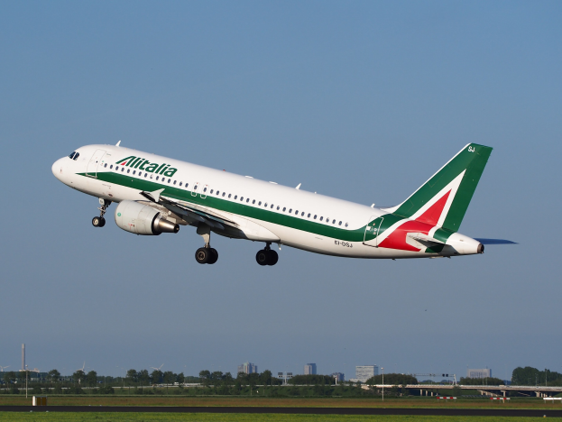 Ein Airbus A320-232 ERJ-EJZ der Alitalia beim Start am Frankfurt Airport mit grünem Gras darunter, Bäumen und Gebäuden im Hintergrund und einem klaren blauen Himmel.