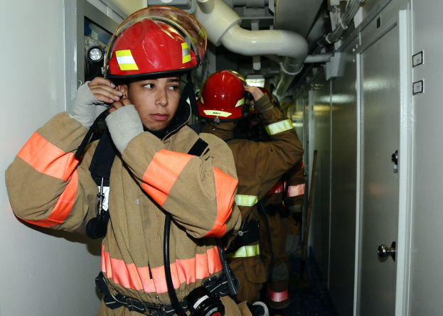 Feuerwehrleute in Uniform, die zusammen in einem Übungsraum mit Rohren und Equipment im Hintergrund stehen.